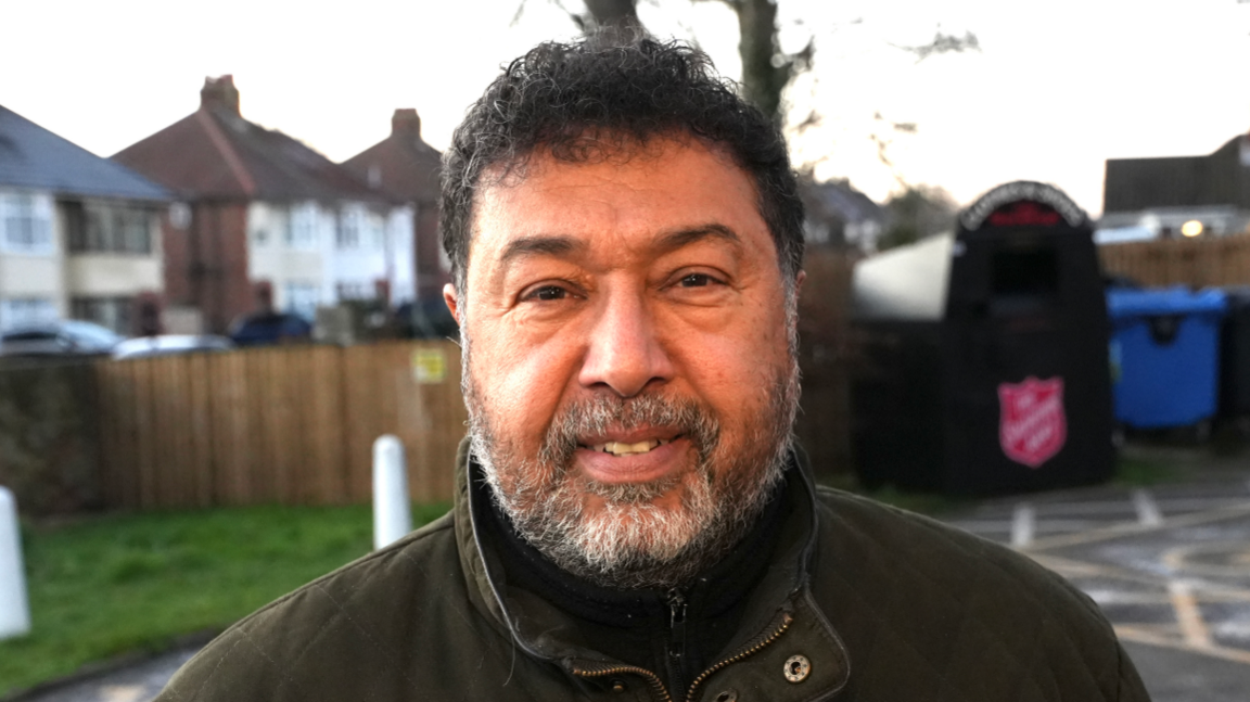 A man with short black hair and grey facial hair. He is smiling into the camera.