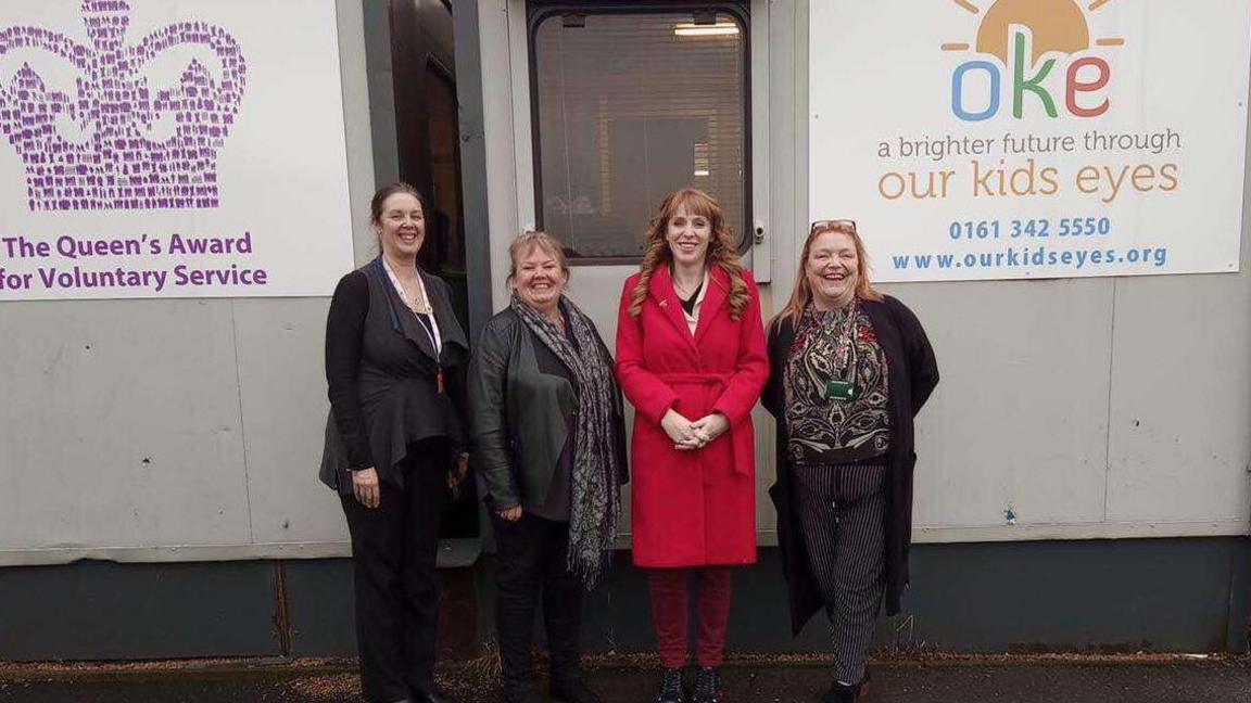 Volunteers from Our Kids Eys stand next to constituency Angela Rayner outside a grey office extension block, which bears a sign with the charities name.