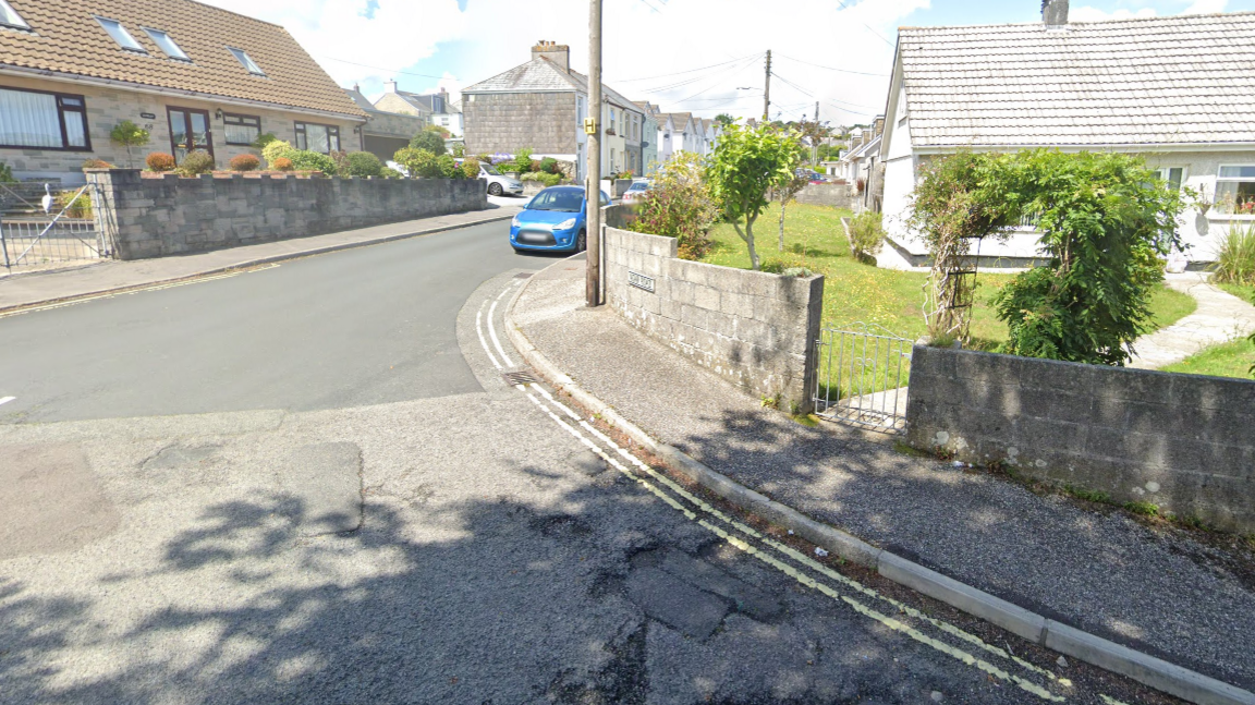 A road junction with houses on the left and right and a car on the right, the car is blue