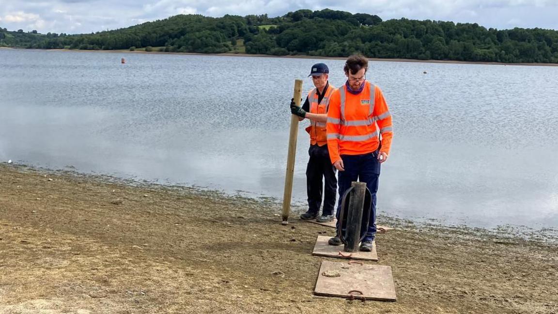 Two men working to install fence posts on the edge of a reservoir