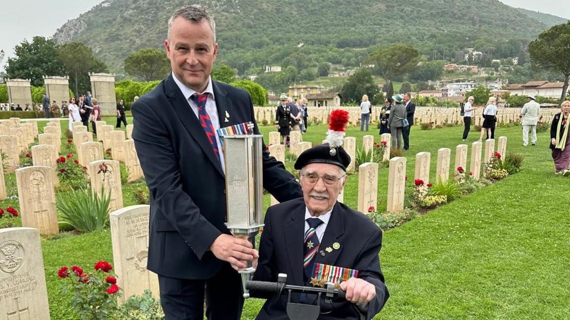 John Hearn holding the torch of commemoration with Jack Hearn seated on a scooter next to him 