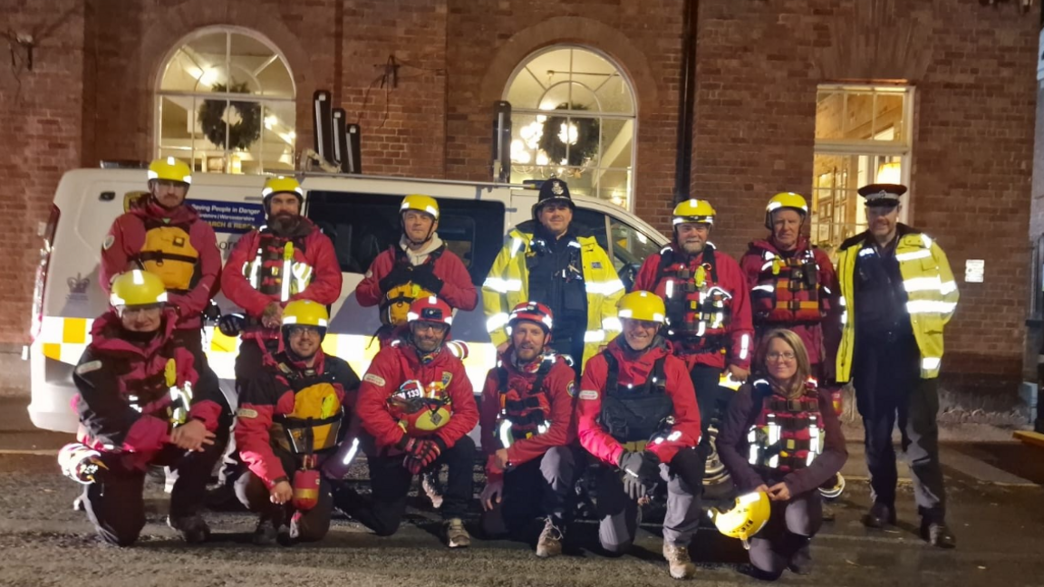 The team and two police officers pose for a photo in uniform by a large white van.