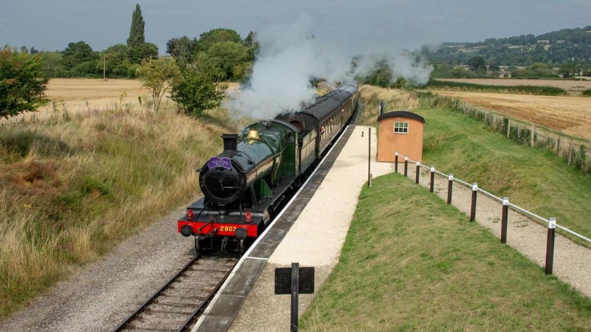 An old fashioned steam locomotive going through green countryside.