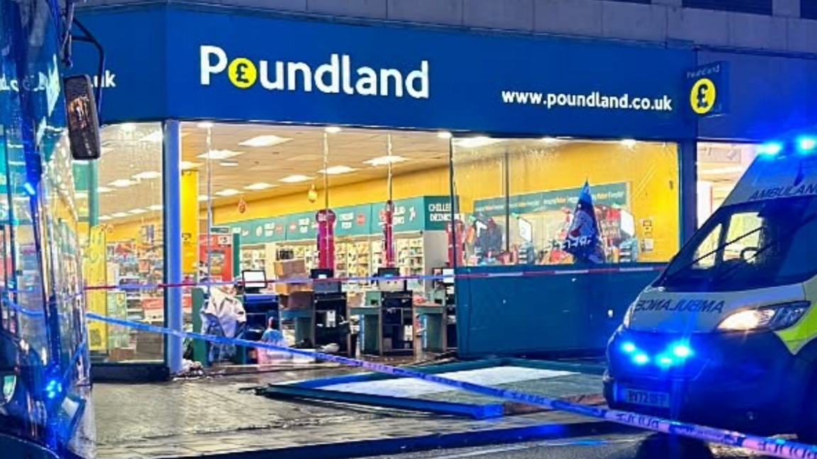 The front of a Poundland store with a broken window lying in the street and an ambulance parked outside, with blue and white police tape around it