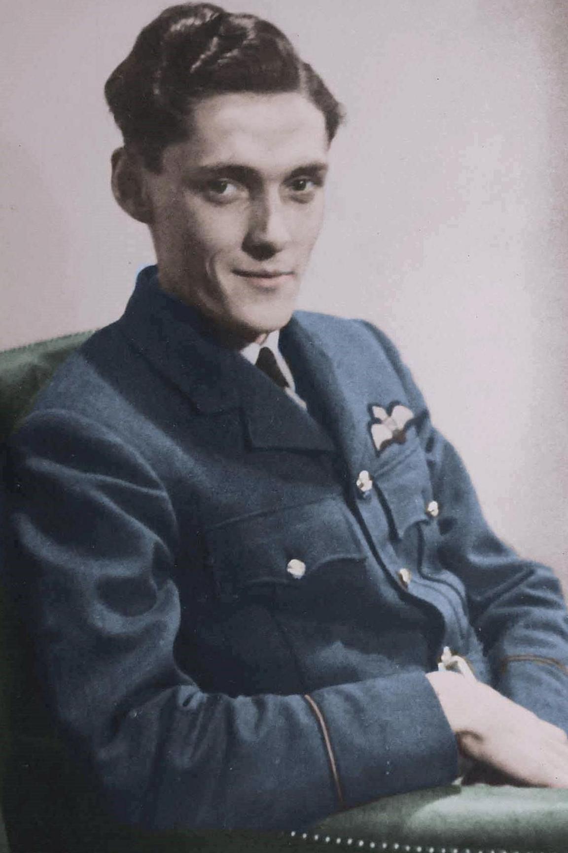 Pete Le Brocq is sitting in a chair smiling a the camera. He has wavy dark hair and is wearing a RAF uniform.