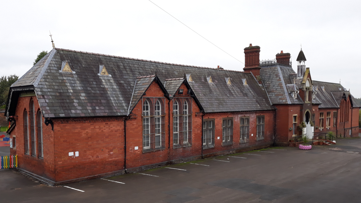 A Victorian building made out of red brick with tall pointed windows and a bell tower.