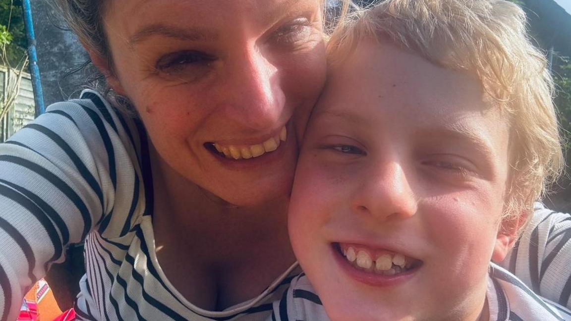 A selfie of Tracy Harris, who has her blonde hair tied back and is wearing a black and white striped top, with her her eight-year-old son Hartley who has blonde hair and is also wearing a black and white striped top. Both are smiling.