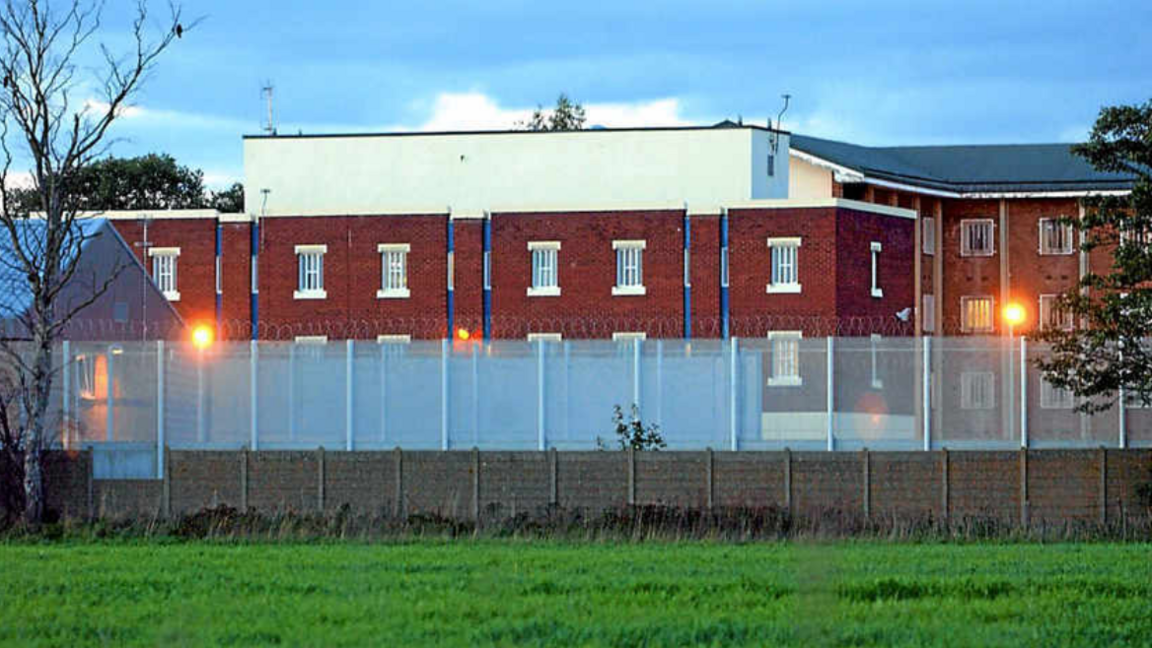 A three-storey building with barred windows, surrounded by a high fence