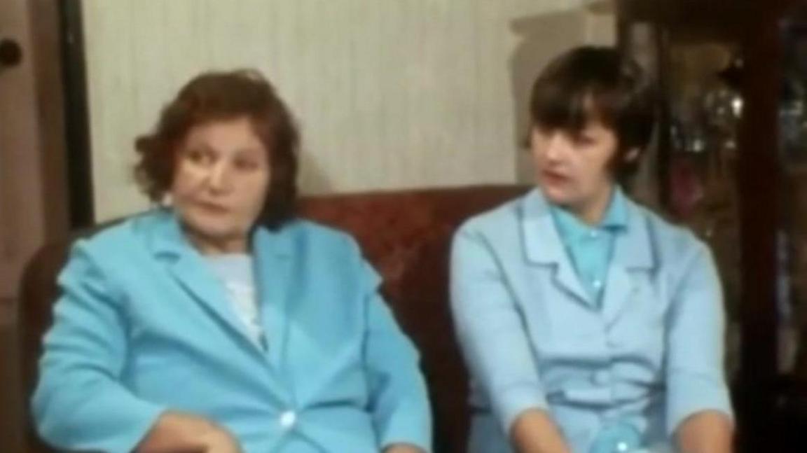 Two women wearing blue  on a sofa in a news report at the time