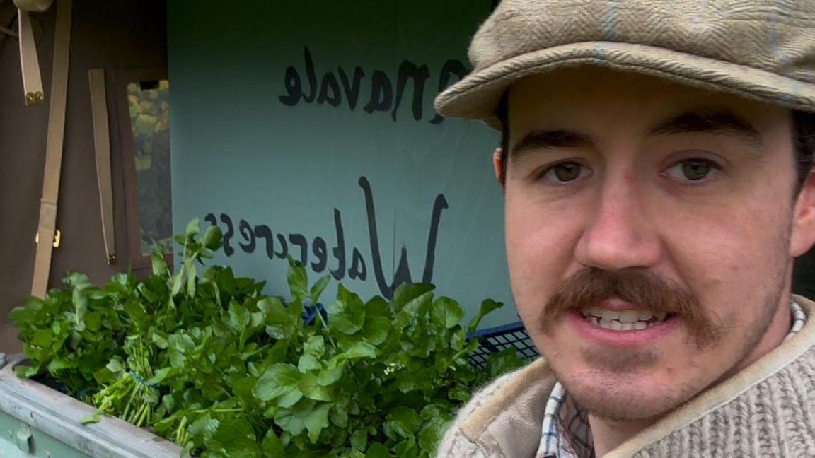 Calvin Hooper, who wears a beige cap and has a brown moustache, stands next to a stall with bunches of watercress on display