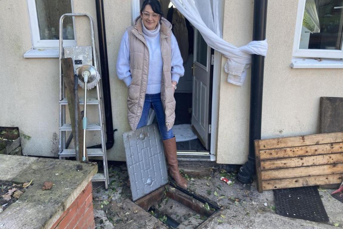 A woman standing next to an open drain near her home