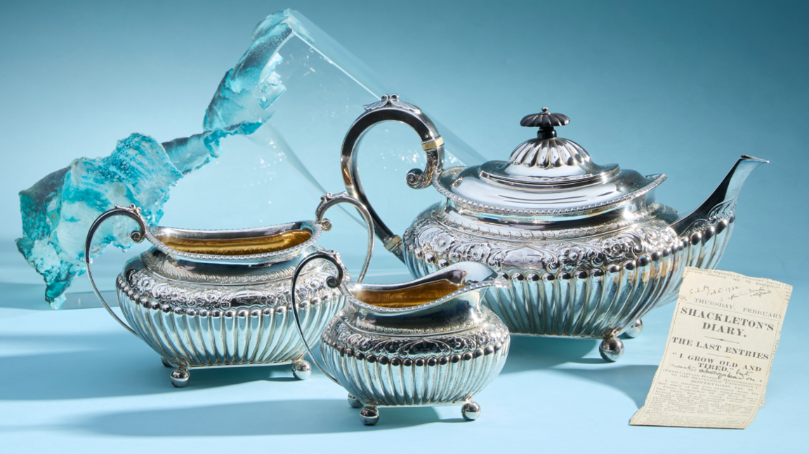 The silver set against a light blue background. It is finely detailed and very shiny. Each piece has an arched handle and little stumps on the bottom.