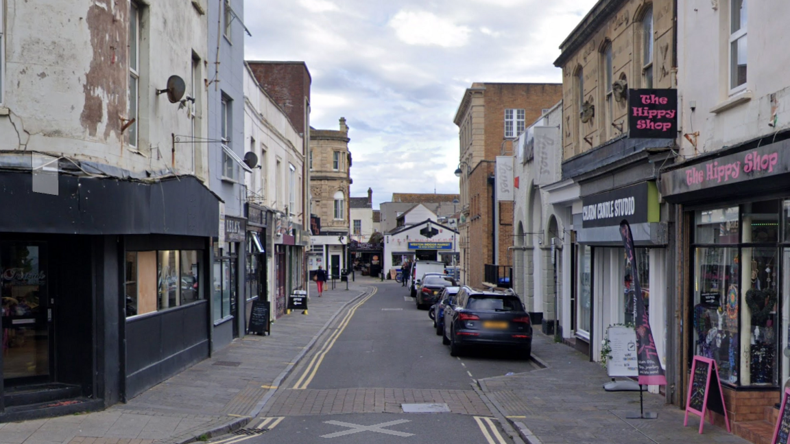 A Google maps street view of West Street in Weston-super-Mare. There are businesses either side of the street and cars parked on one side of the road.