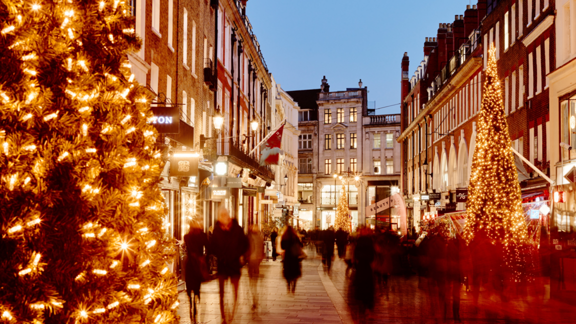 A street of shops decorated for Christmas, with a large tree in the foreground.