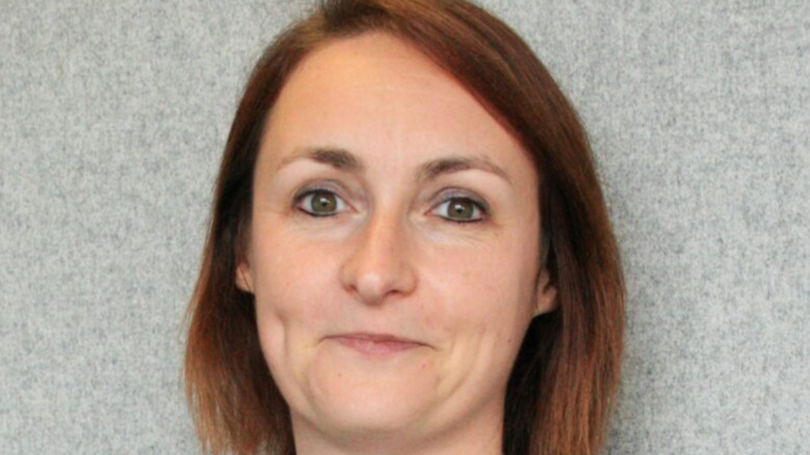 A lady with shoulder-length brown hair is smiling at the camera in a close-up photo.