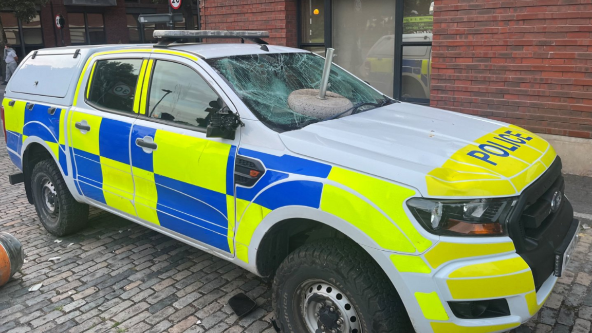 A vandalised police vehicle with an object thrown at its windscreen