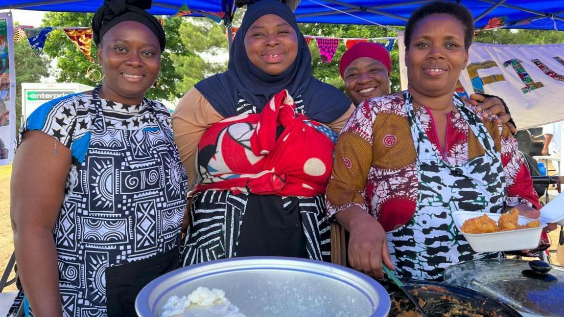 From left to right Ltoya Augustt, Fati Tourau,Sadiya Abdullahi and Ivon Kayitesi of the African food stall smiling for the camera and putting food in containers.