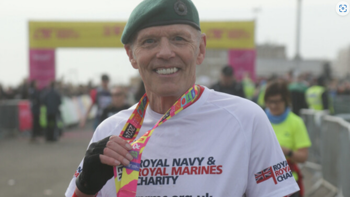 Chris Terrell having completed the Brighton Marathon, walking on crutches through the streets of the city. He is wearing a brightly coloured and logoed t-shirt and a green Royal Marines beret.