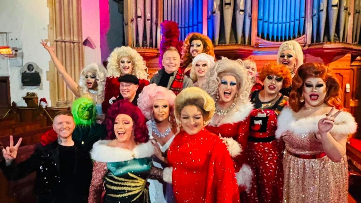 Drag queens stand in front of a church organ.