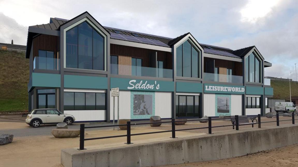 A CGI for the new amusement centre. The building is modern and has a number of large windows overlooking the beach. It is white and blue and has solar panels on the roof. Three apartments are on the upper level.