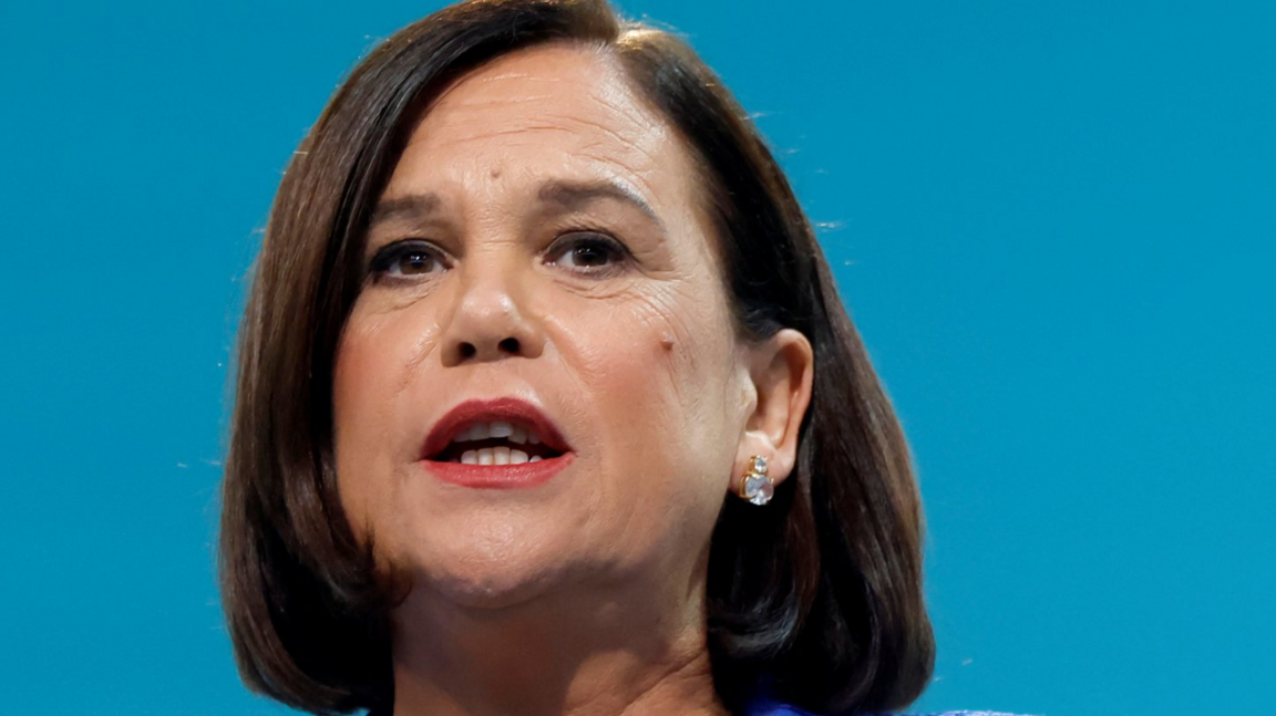 Mary Lou McDonald making a speech with a blue background behind her. 