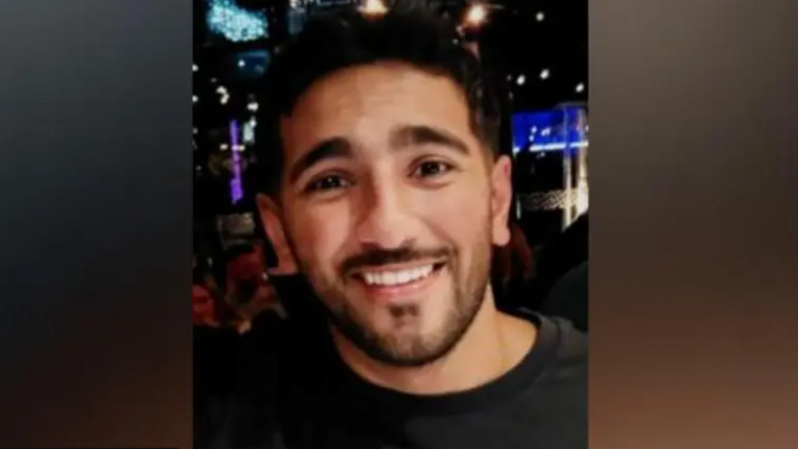 Dyn 28-oed gyda gwallt tywyll yn gwenu at y camera.