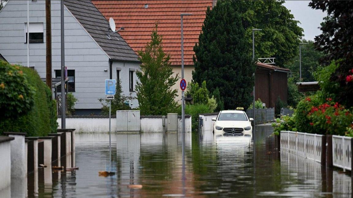 A photo of a flooded street in southern Germany with water up to a car's radiator