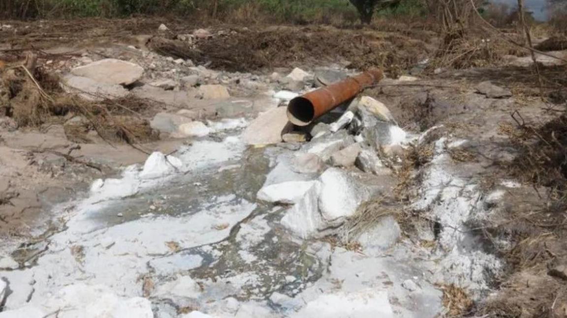 A pipe leading to a dry river. The rocks are covered in a white sediment