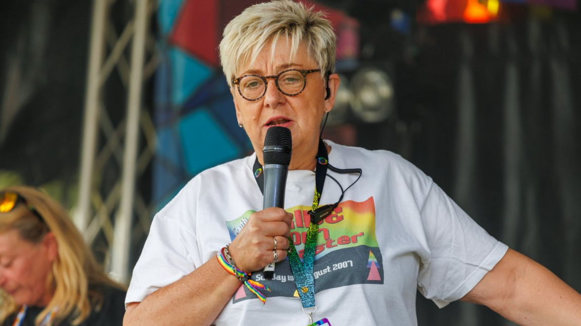 Woman with short blonde hair and glasses on stage with a microphone