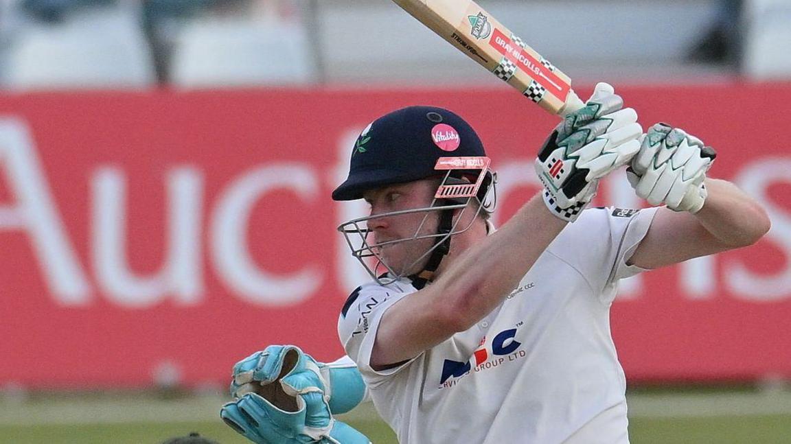 Matthew Revis batting for Yorkshire with a helmet on with wicket-keeper gloves visible behind him