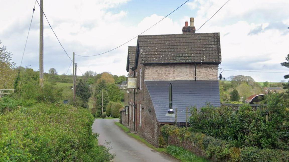 A Google street view image of an old pub building next to a rural road in the middle of the countryside.