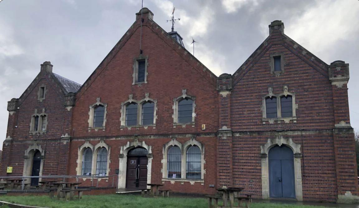 An imposing brick building with 12 arched windows and three arched doors.