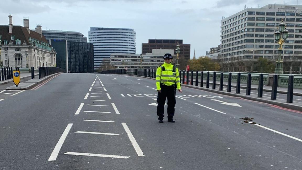 A police officer, wearing an illuminous jacket and black trousers, stands on a deserted Westminster Bridge 