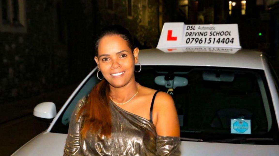 A woman smiles while sitting on the bonnet of a silver car. 