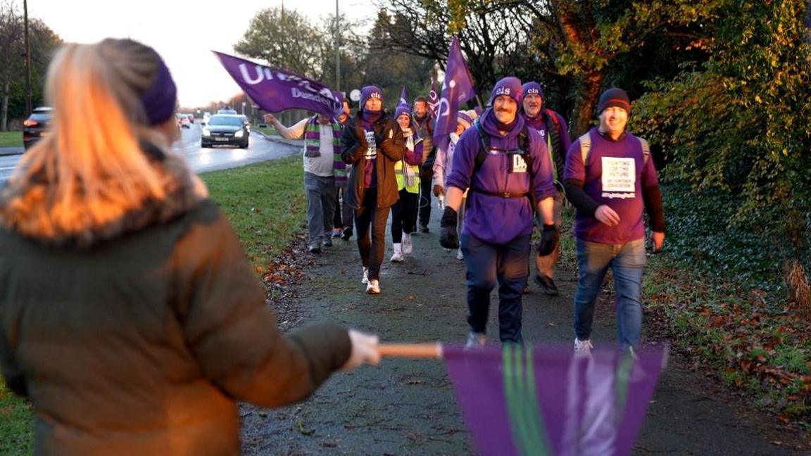 Dundee and Angus College staff and students waving purple flags, walking along a pavement.