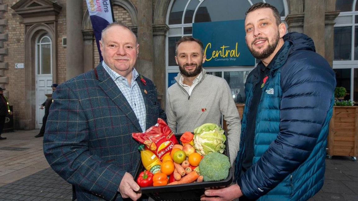 Three men hold a box of food outside the Queen's Building in Wolverhampton