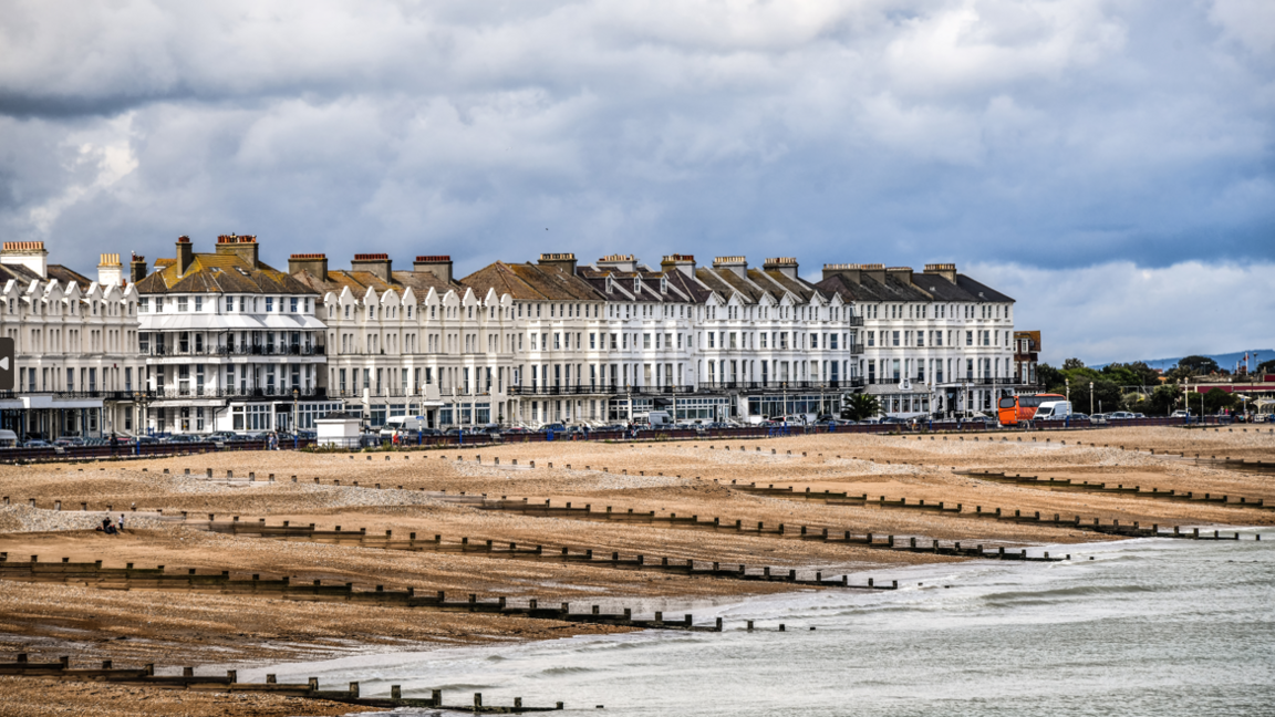 A landscape view of Eastbourne beach, showing groynes and seafront housing on an overcast day.