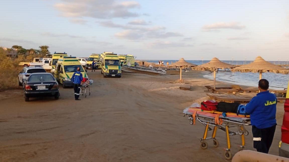 On the beach, medic with a stretcher loaded with supplies on the bottom right. In the top left, multiple ambulance vans and some cars.