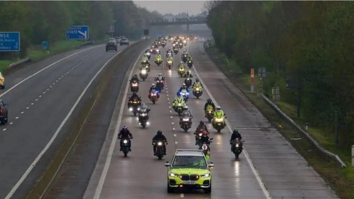 A police car being followed by a convoy of motorbikes on the motorway