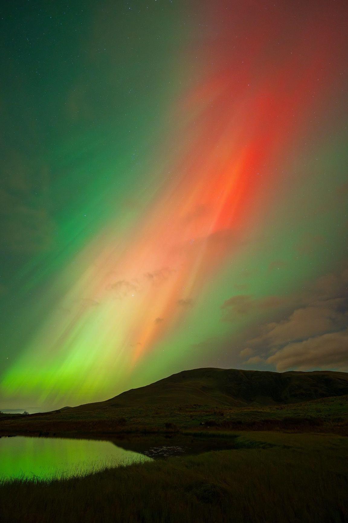 Red and green lights in the sky above a tarn.