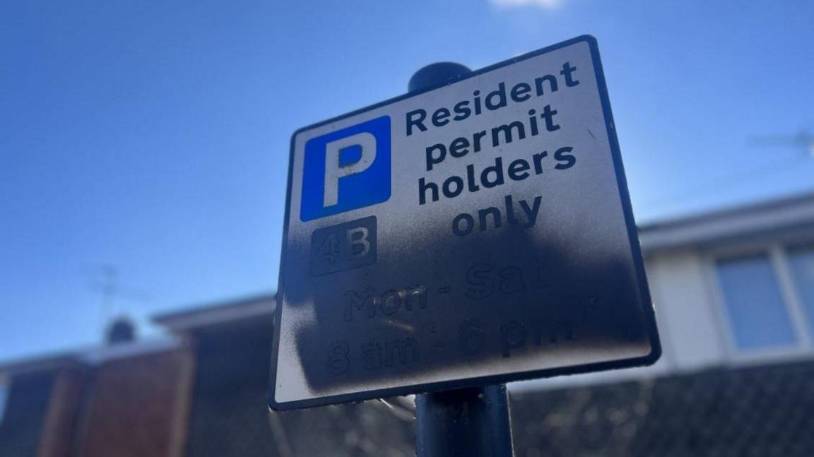 A parking sign reading 'Resident permit holders only' but half of the sign is spray-painted with black spray paint.