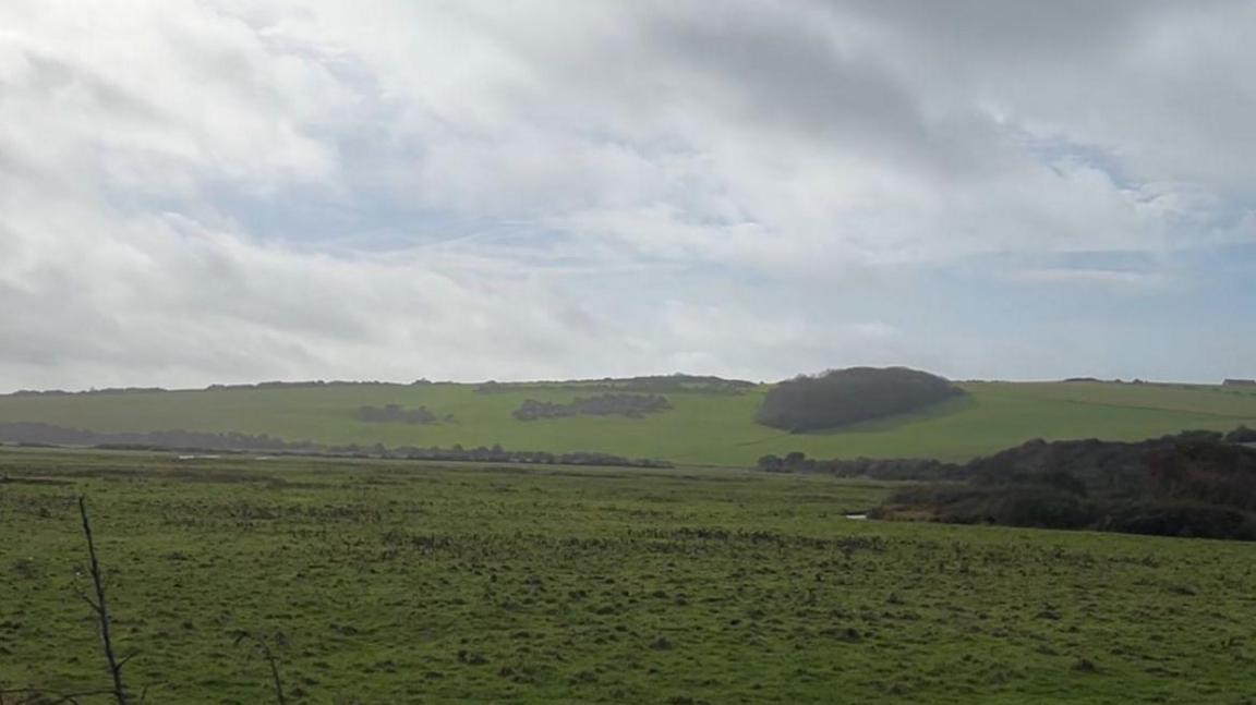 A large expanse of fields with gradual hills in the background. This section is protected by a river bank