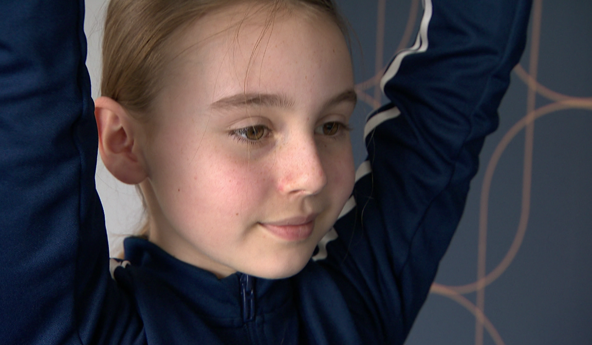 Amelia getting ready to perform a trick. Her arms are in the air. She is wearing a navy track-suit.