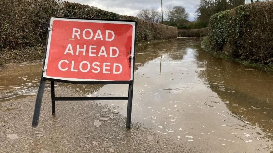 A road flooded with surface water and a red sign to say road closed