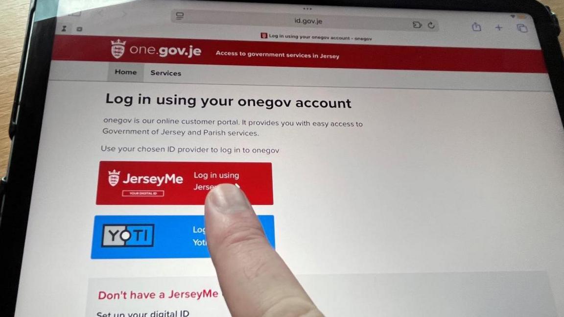 A finger touches a red Log On button the Jersey tax return website, displayed on a tablet.