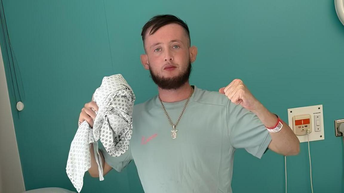 Man wearing grey clothing standing next to a bed