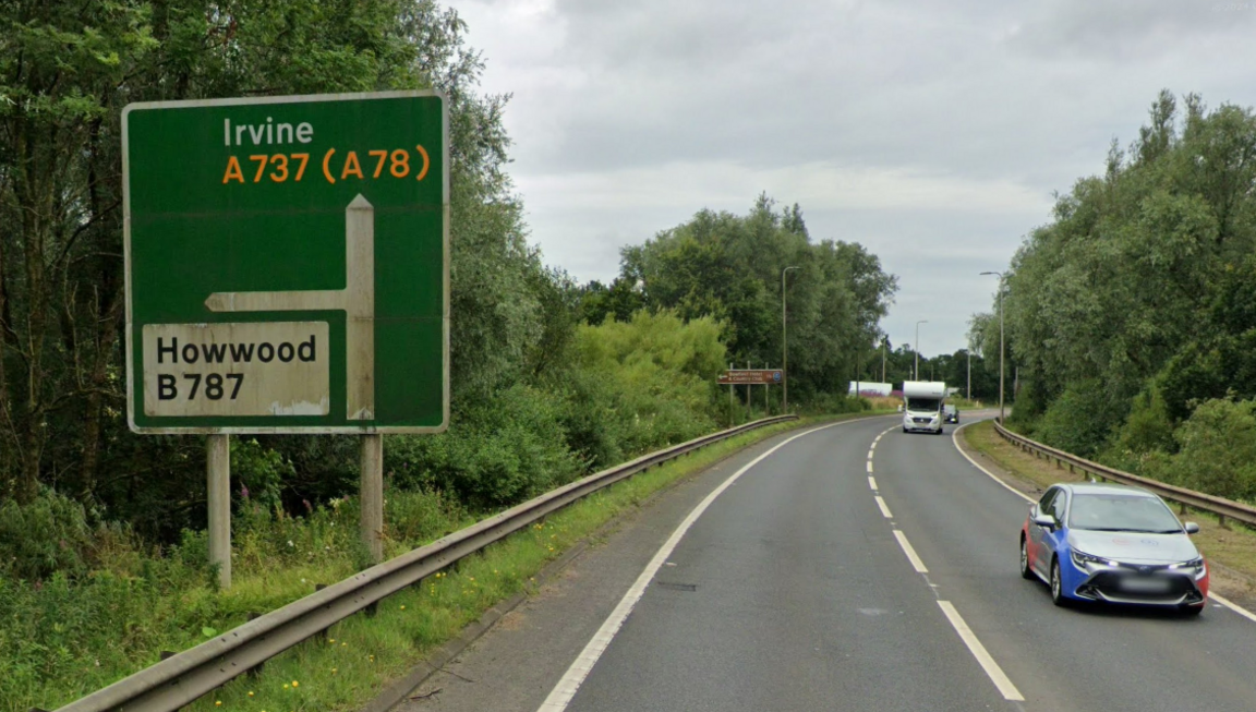 Image shows green road sign with Howood and Irvine on it. There is a car and a motorhome visible on the road.