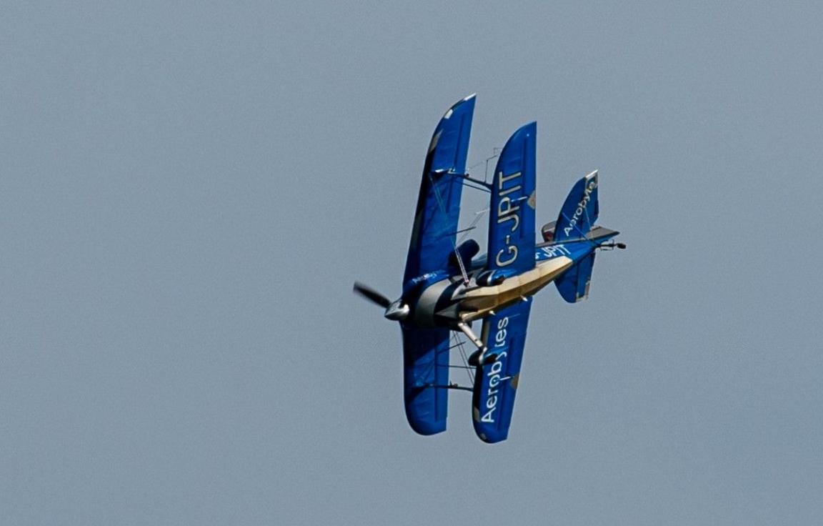 A blue Pitts bi-plane bearing the callsign G-JPIT performing a steep turn in the sky