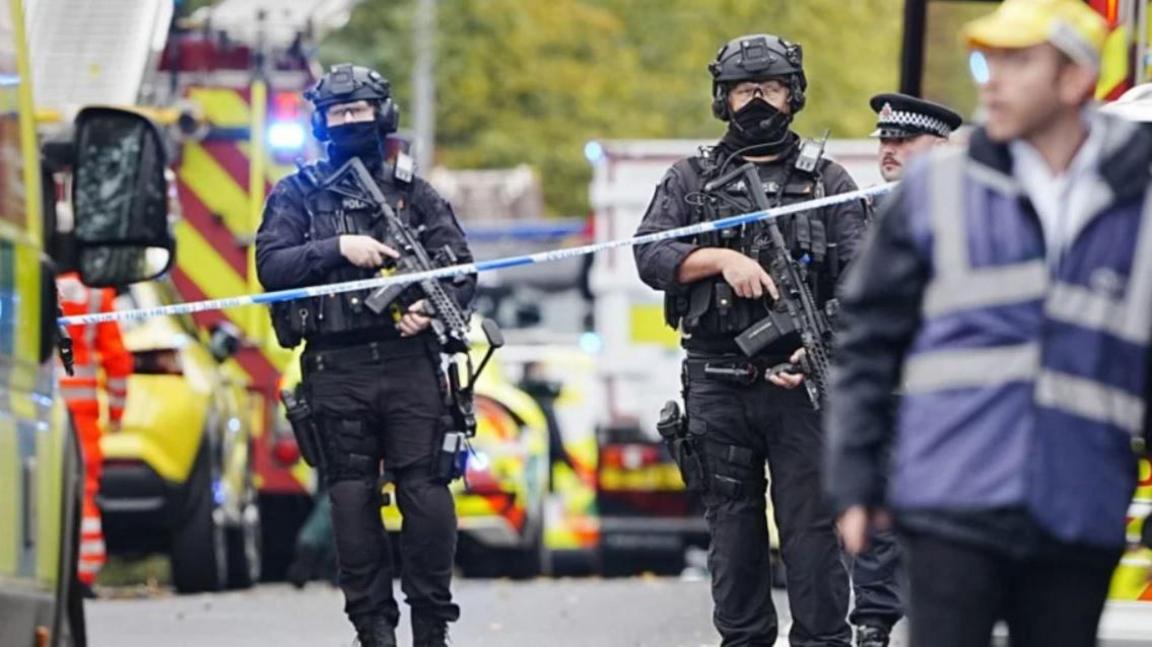 Armed police at the scene, with police vehicles in the background.