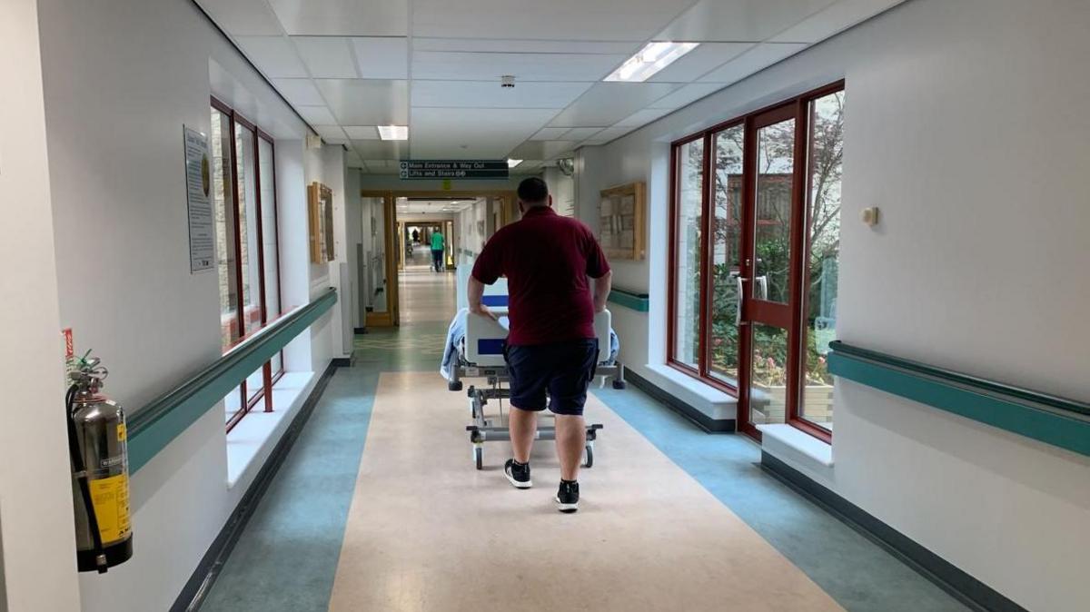 A man pushing a hospital bed through a hospital corridor